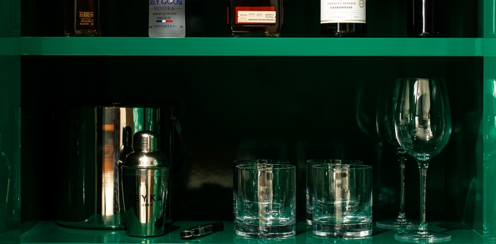 Multiple Bottles on Three Green shelves of Wet Bar in Hotel