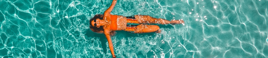 Aerial shot of woman floating on back in pool water in orange bikini